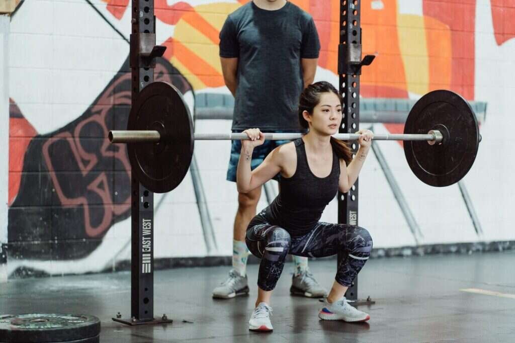 Coach guiding a client through a weighted squat in a gym