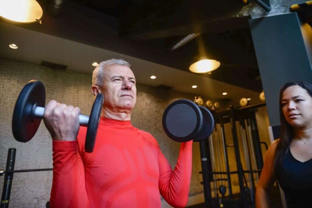 Coach guiding an older adult through a dumbbell lift at a strength training facility