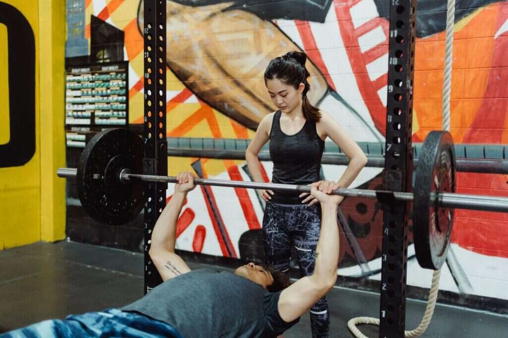 A coach guiding a lifter through a bench press, the session already planned before the client arrived