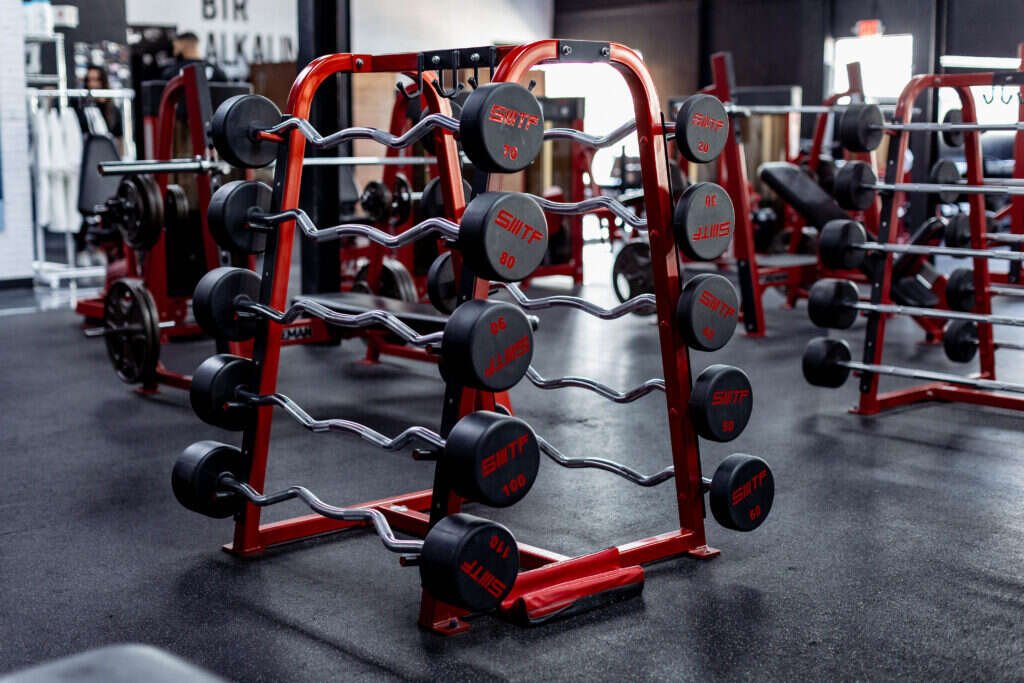 Loaded barbell racks and free weights on the training floor of a private Dallas strength facility