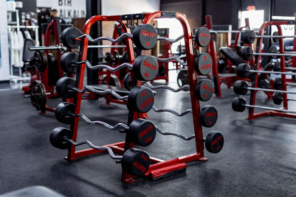 Loaded barbell racks and free weights on the training floor of a private Dallas strength facility